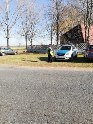 Na zdjęciu widoczny umundurowany policjant w trakcie akcji Znicz. Zdjęcie wykonane na tle cmentarza.