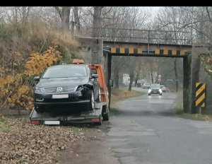 Na zdjęciu widoczny samochód osobowy koloru ciemnego z widocznymi uszkodzeniami w przedniej części, wynikających z udziału w kolizji.