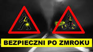 Na zdjęciu widoczny nieoświetlony odcinek drogi publicznej, na której znajdują się ikonografie rowerzysty oświetlonego i ubranego w elementy odblaskowe oraz nieoświetlonego.  Poniżej napis BEZPIECZNIE PO ZMROKU