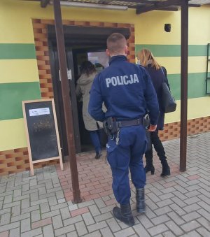 Na zdjęciu umundurowany policjant, w asyście pracowników SANEPIDU w trakcie kontroli przestrzegania obostrzeń związanych z COVID -19