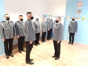 Na zdjęciu widoczni ubrani w mundury galowe policjanci w trakcie uroczystości. Zdjęcie wykonane wewnątrz pomieszczenia.