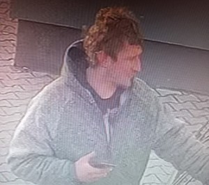 Na zdjęciu widoczny sprawca kradzieży samochodu osobowego, który wchodzi do sklepu. W ręku trzyma telefon komórkowy.
