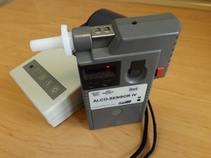 Na zdjęciu widoczne urządzenie służące do badania kierujących na zawartość alkoholu w wydychanym powietrzu. Tuż obok urządzenia widoczna drukarka.