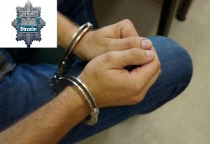 Zdjęcie zawiera dłonie zatrzymanej osoby, na które założone są kajdanki. W lewym górnym rogu znajduje się logo Kolmendy Powiatowej Policji w Strzelinie.