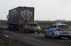 Na zdjęciu widoczny ciągnik siodłowy wraz z naczepą w trakcie kontroli drogowej przeprowadzanej przez umundurowanych policjantów.