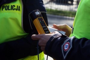 Na zdjęciu widoczne dłonie umundurowanego policjanta, w których trzyma urządzenie do pomiaru zawartości alkoholu w wydychanym powietrzu.