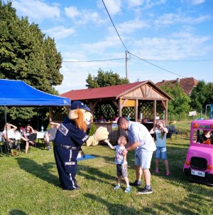 Na zdjęciu widoczne dzieci w wieku szkolnym biorące udziała w zajęciach profilaktycznych odbywających się na terenie placu zabaw. W tle widoczni umundurowani policjanci oraz maskotka Komisarz Lew.