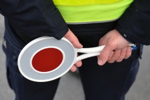 Na zdjęciu widoczne dłonie umundurowanego funkcjonariusza ruchu drogowego, który w rękach trzyma tarczę (&quot;lizak&quot;) służący do zatrzymywania pojazdów.