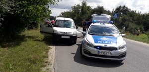 Na zdjęciu widoczny radiowóz oznakowanego tuż obok pojazd dostawczy koloru jasnego. W tle umundurowani policjanci wykonujący czynności służbowe.