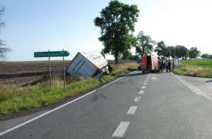 Na zdjęciu widoczne miejsce wypadku drogowego, ciągnik siodłowy wraz z naczepą leży w rowie przechylony na lewą stroną. Na odcinku drogi obrócony tyłem do kierunku jazdy znajduje się samochód typu bus.