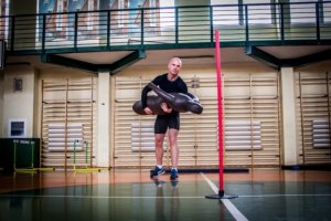 Na zdjęciu widoczny mężczyzna w stroju sportowym w trakcie wykonywania ćwiczeń na sali gimnastycznej.